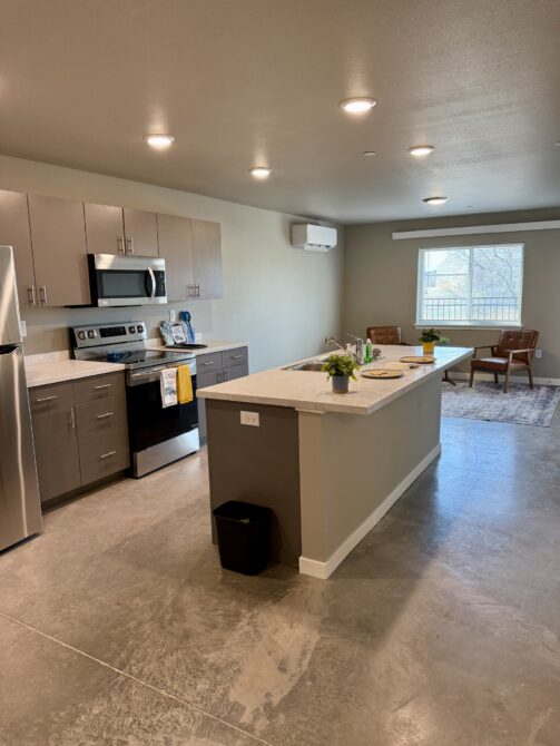 Modern kitchen with center island, stainless steel appliances, dining area, and natural light from large window.