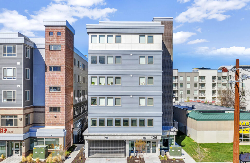 Modern five-story apartment building with brick and gray siding, numbered 426, adjacent to other residential structures.