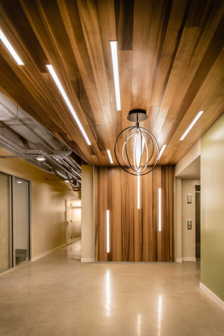 Modern hallway with wooden ceiling, linear lights, and geometric chandelier.