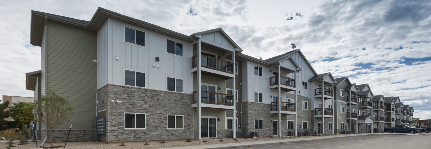 Three-story apartment building with stone façade and balconies under a partly cloudy sky.