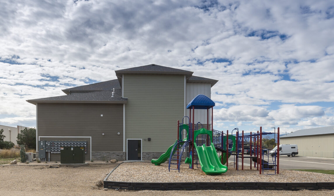 Playground with green slides next to a two-story building under cloudy sky