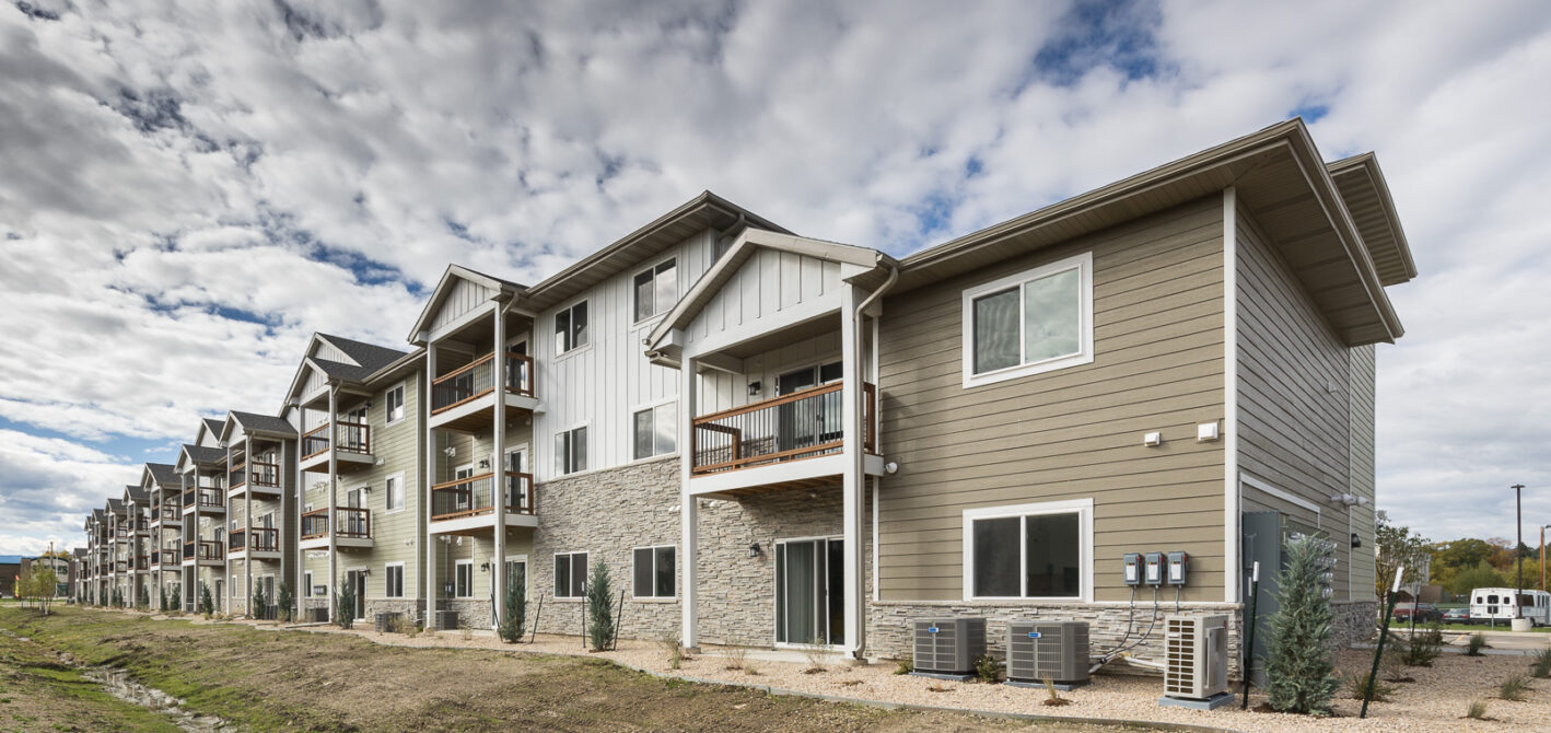 Row of modern three-story apartment buildings with balconies, set against a cloudy sky