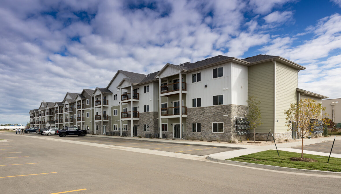 Apartment building with balconies, stone facade, parked cars, and overcast sky.
