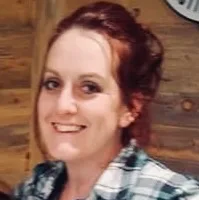 Amanda smiling, wearing plaid shirt, wooden wall background