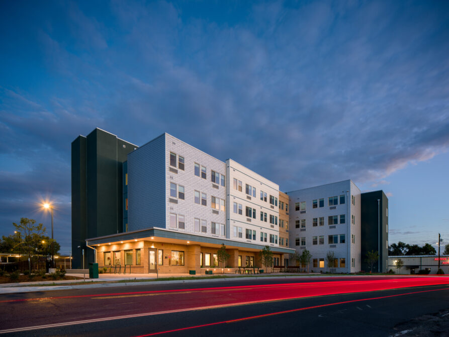Modern multi-story building at dusk with streetlights and a vibrant sunset sky.