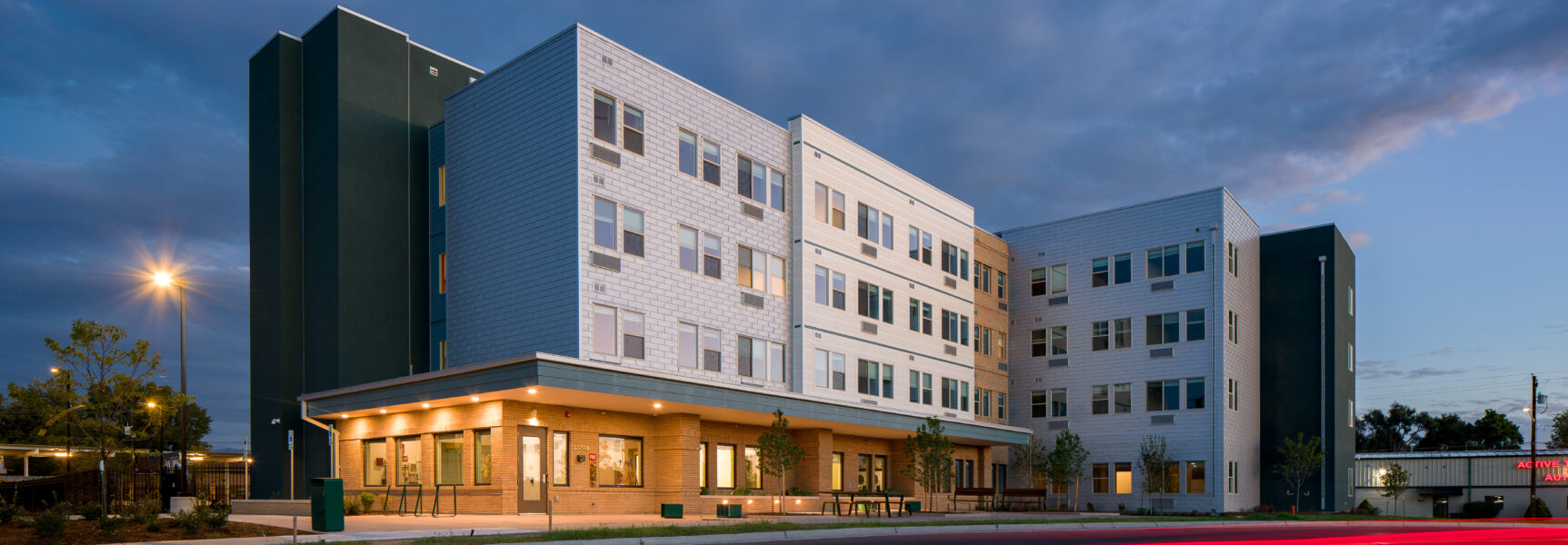 Modern four-story building at dusk with large windows and exterior lighting.