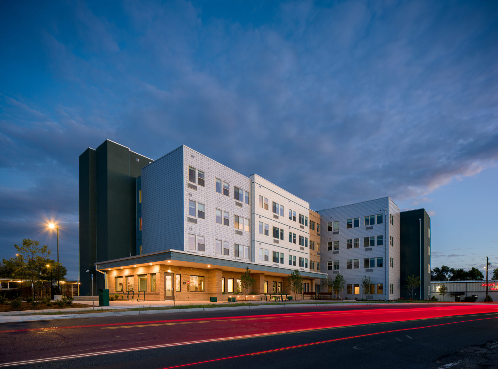 Modern apartment building at dusk with bright streaks from vehicle lights.