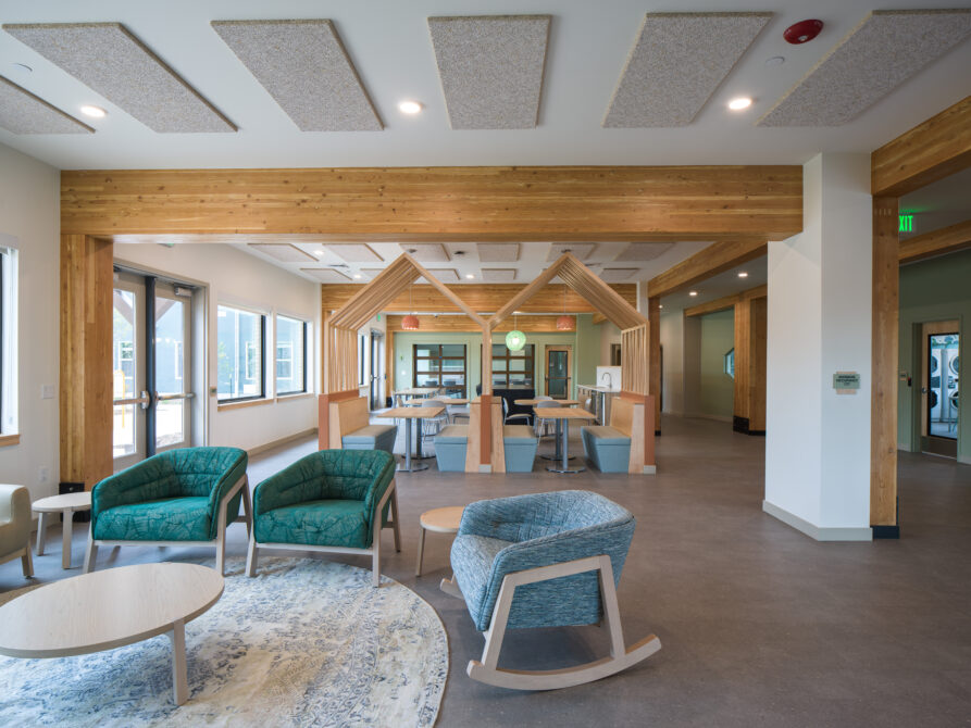 Spacious lounge area with wooden accents, modern chairs, and tables under natural lighting.