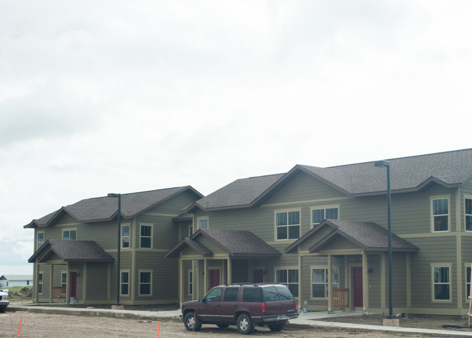 Row of beige townhouses with sloped roofs and parked SUV in foreground