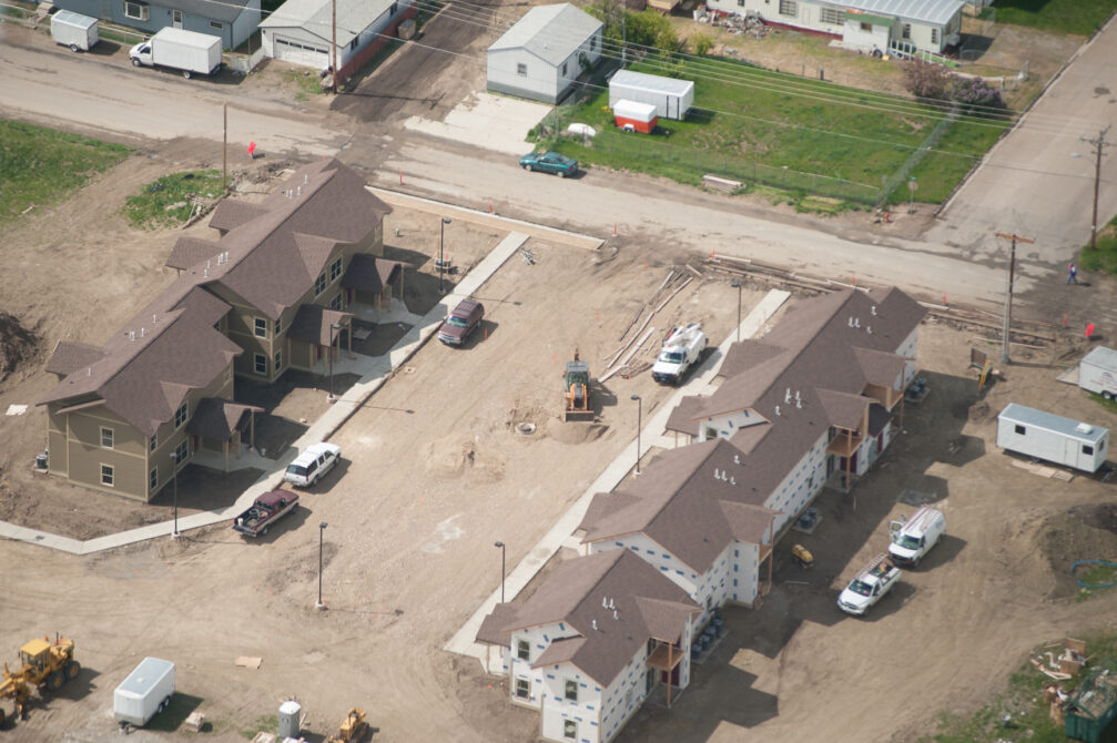 Aerial view of a construction site with two brown-roofed buildings, vehicles, and scattered construction equipment.