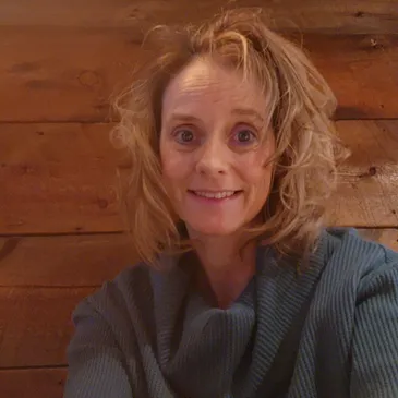 Charlie smiling, wearing a blue sweater against a wooden wall background.