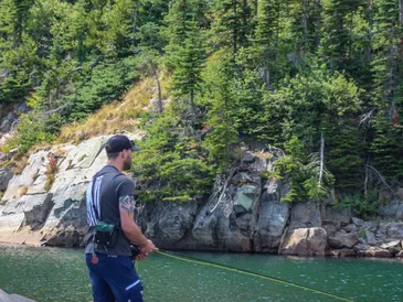 Cody standing by a lake, fishing in a forested area.