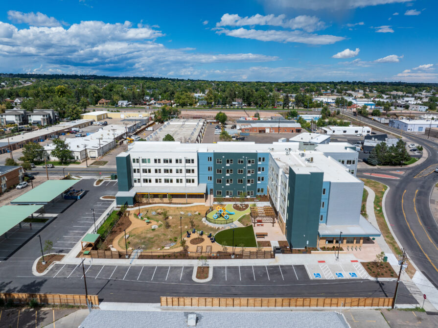 Aerial view of a large, modern apartment complex with a central playground, surrounded by a residential neighborhood and parking area.