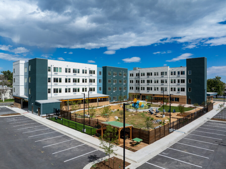 Four-story apartment building with a central playground, surrounded by parking spaces.