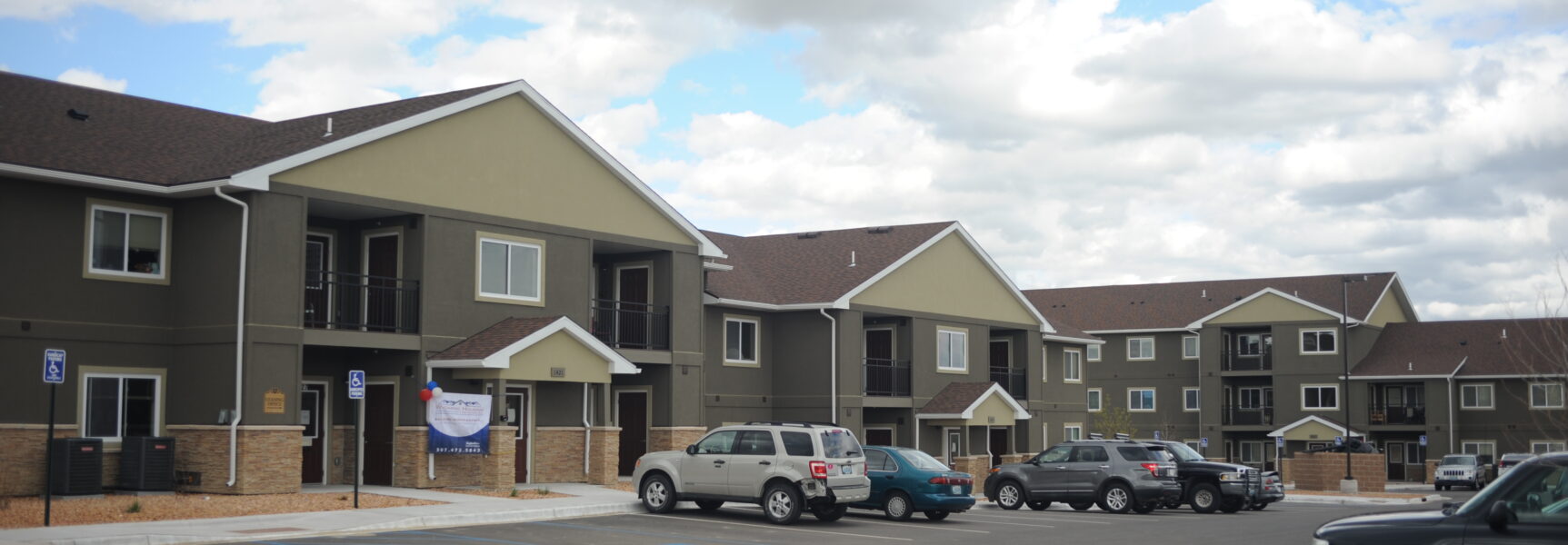 Apartment complex with cars parked in front, gray exterior, and accessible parking signs visible.