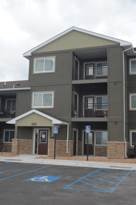 Three-story apartment building with balconies above accessible parking spaces