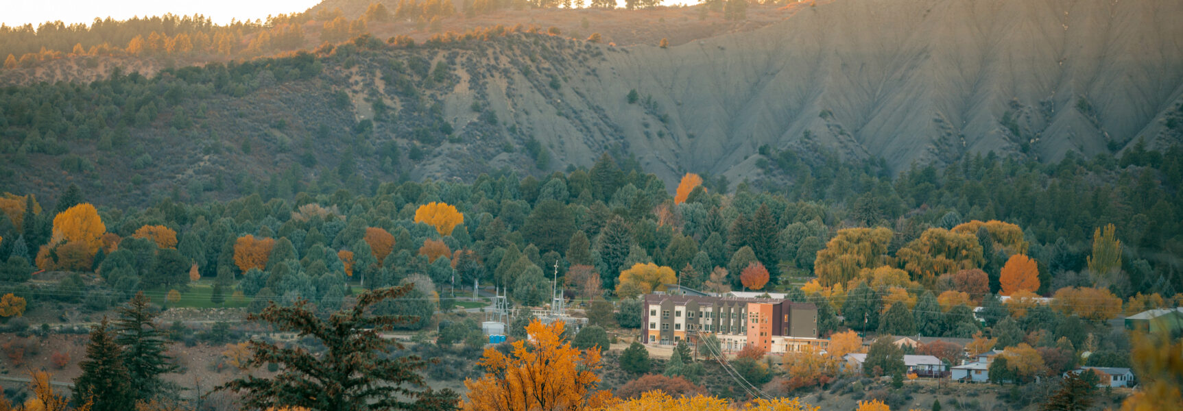 Mountainous landscape with autumn trees surrounding a building complex, displaying vibrant orange and green foliage.