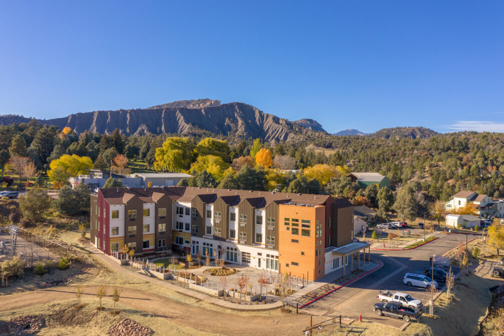 Multiple-story residential building with colorful facade, surrounded by trees and mountains under clear blue sky