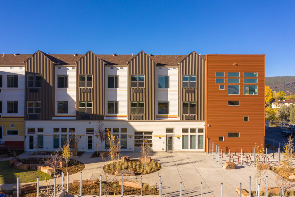 Modern three-story building with striped facade and large windows against a clear blue sky