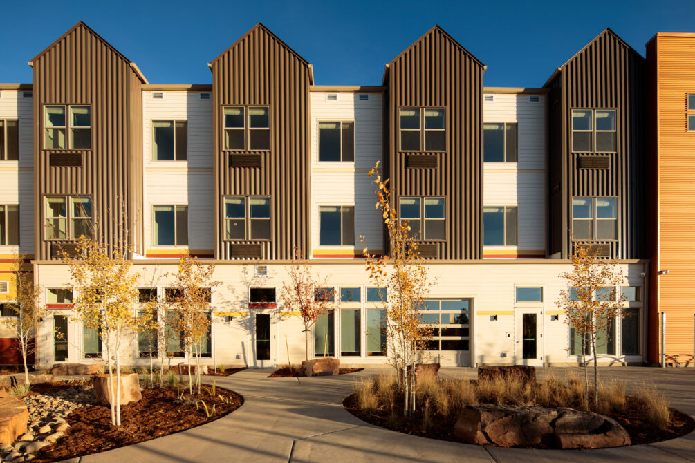 Modern apartment building with gabled roofs and large windows, surrounded by young trees and landscaped grounds.