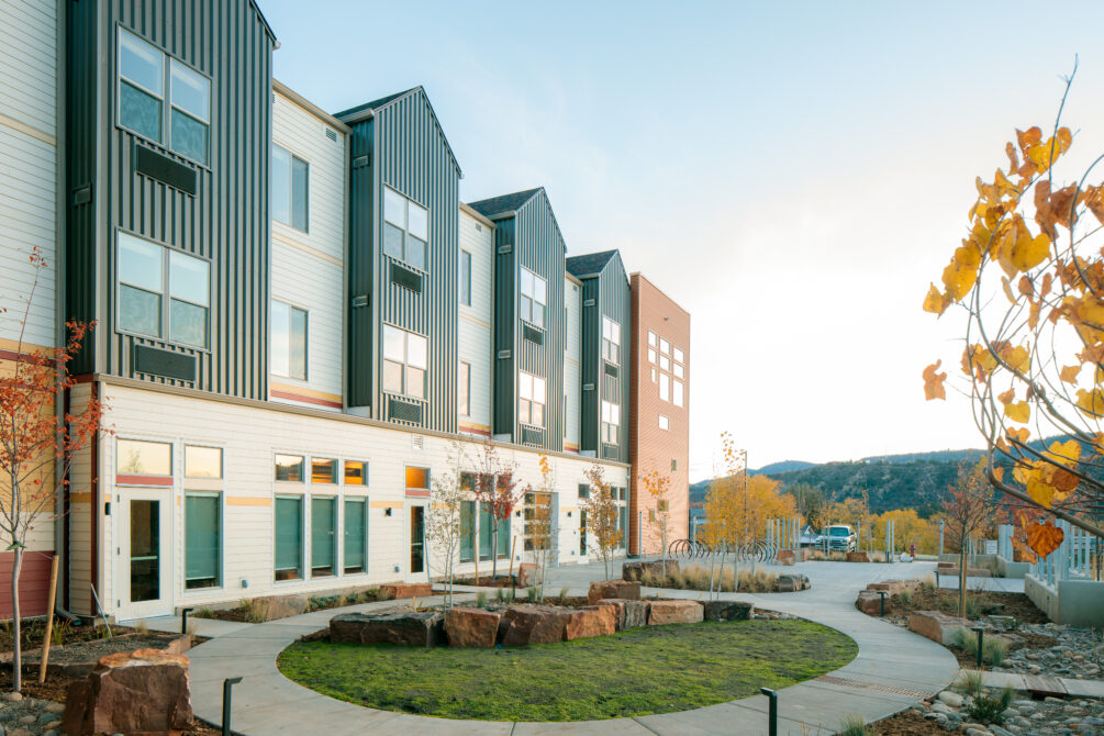 Modern building with black and white siding, surrounded by landscaped pathway and autumn trees.