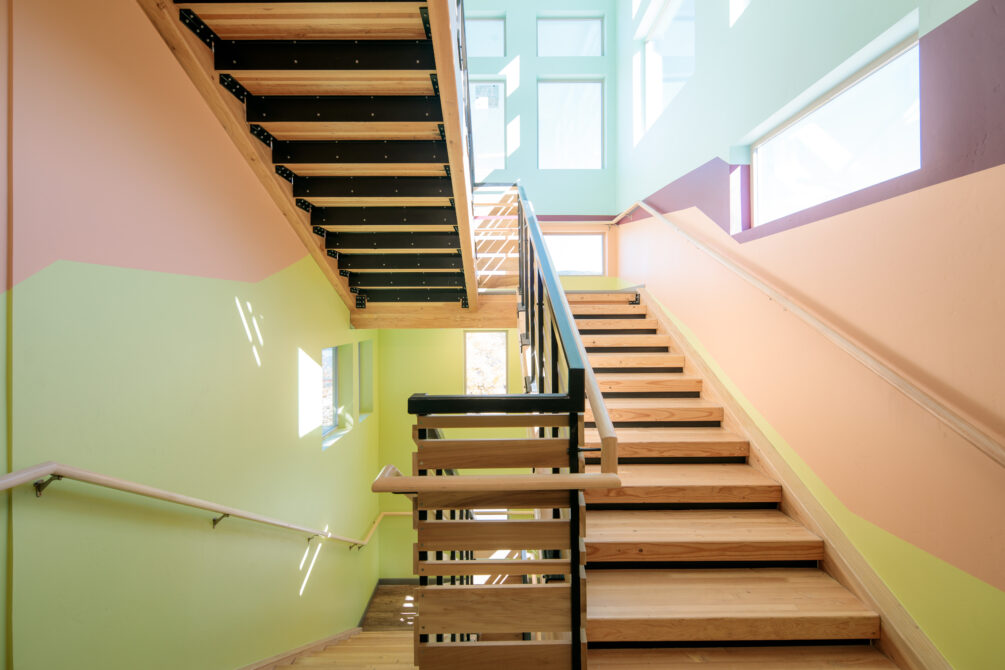 Colorful, multi-level staircase with soft pastel walls and wooden steps, well-lit by windows.
