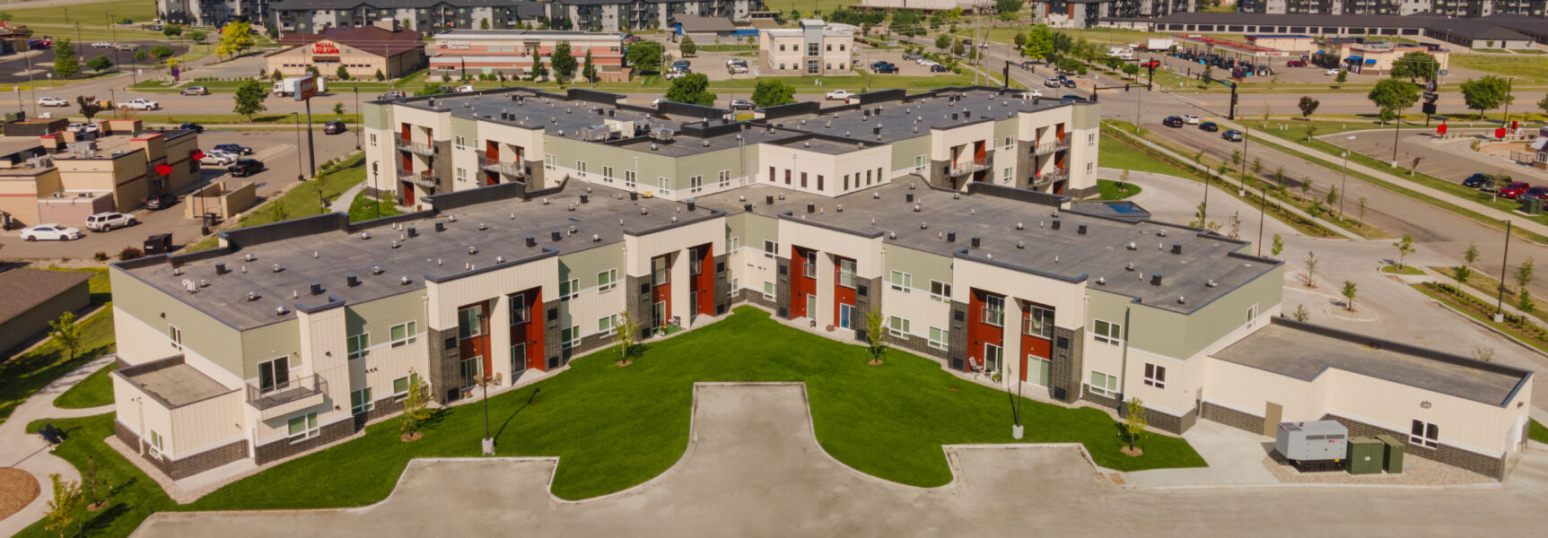 Aerial view of a large, modern residential complex with green lawns, surrounded by roads and other buildings.