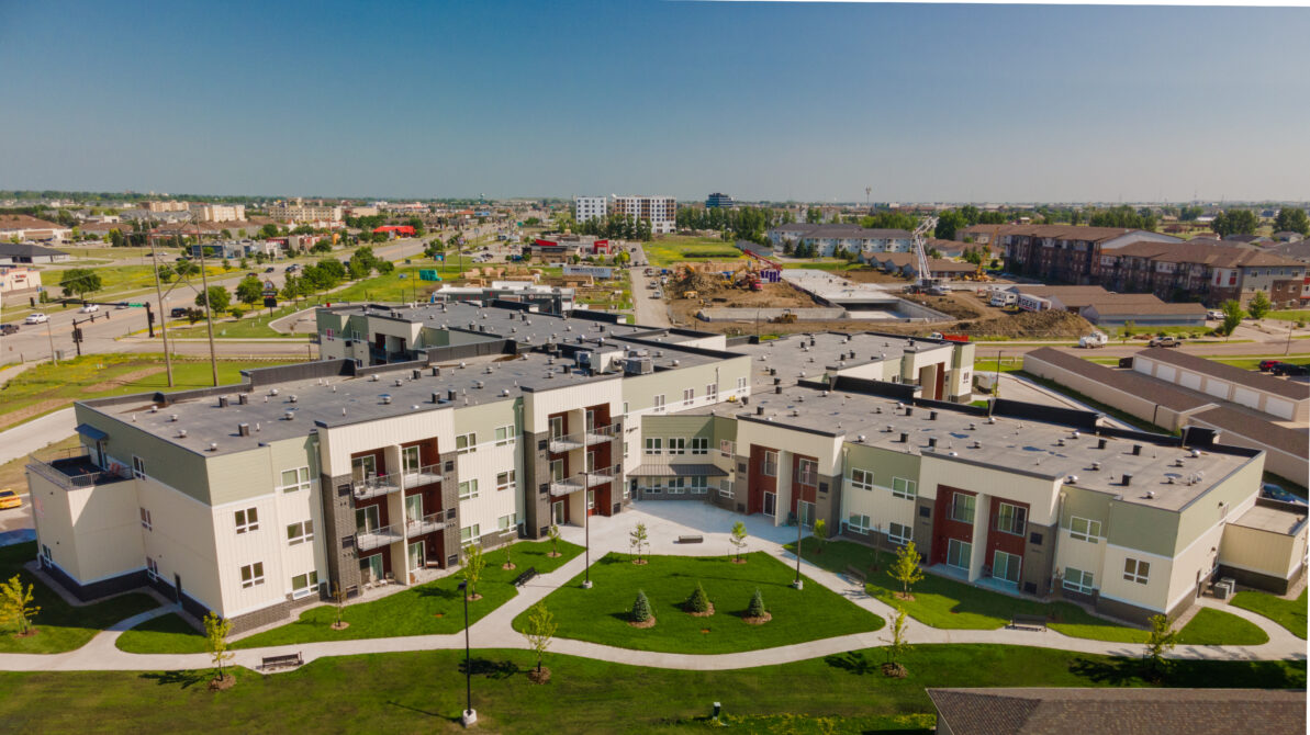 Aerial view of a large apartment complex with green lawns and nearby commercial and residential areas.