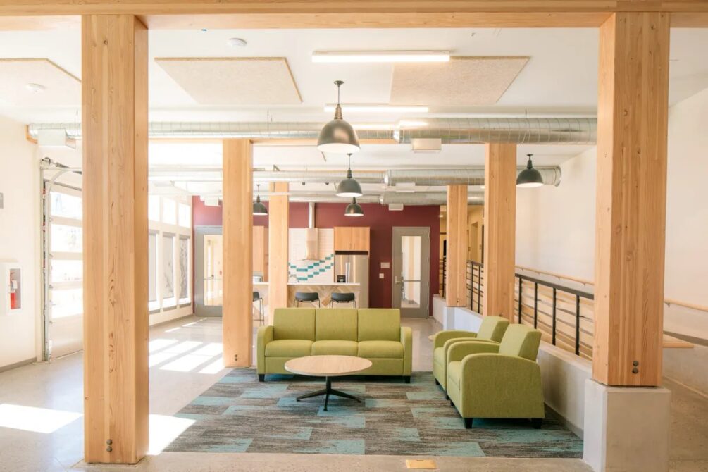 Spacious modern room with green sofas, wooden beams, and industrial lighting.