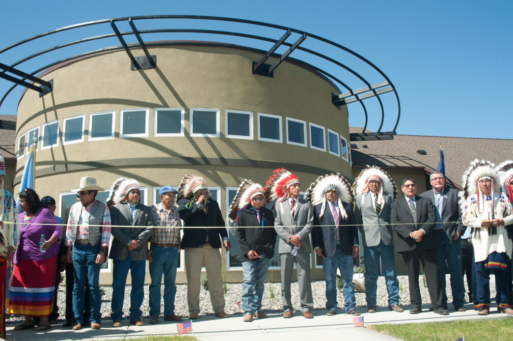 People in ceremonial attire stand in front of a modern building, participating in a grand opening ceremony.
