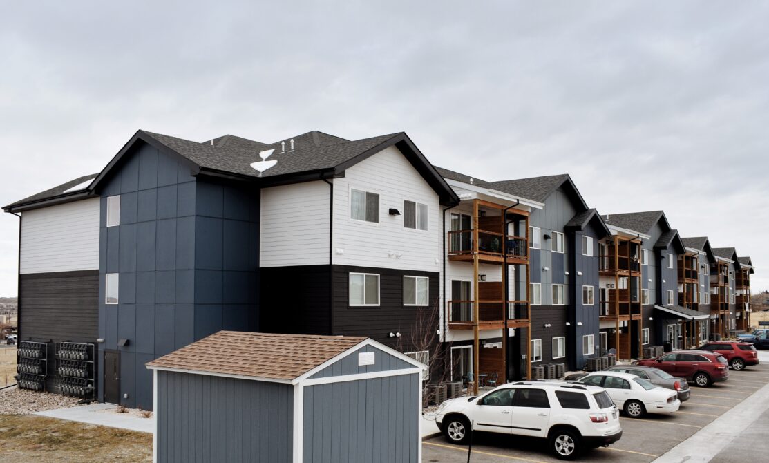 Modern apartment complex with balconies, cars parked in front, and cloudy sky overhead