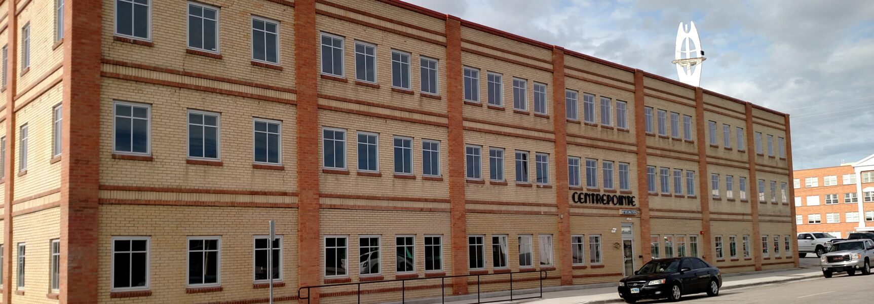 Three-story brick building labeled "CENTREPOINTE" with parked cars in front