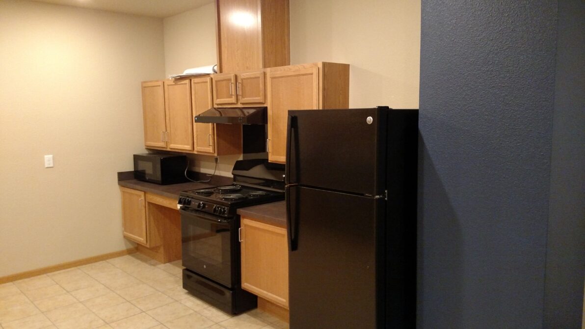 Kitchen with oak cabinets, black appliances, including a stove and refrigerator, beige walls, and tiled floor