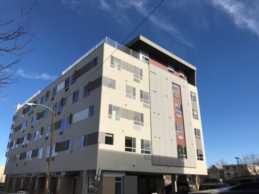 Modern multi-story apartment building with a flat roof against a clear blue sky.