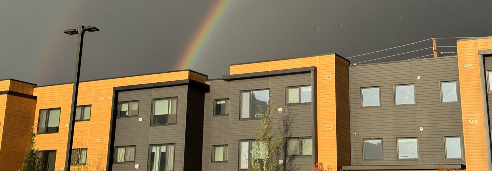 Rainbow arches over modern-style buildings against a dark sky.
