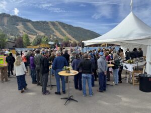 People gathered at a mountain themed outdoor event with tables and a white tent.