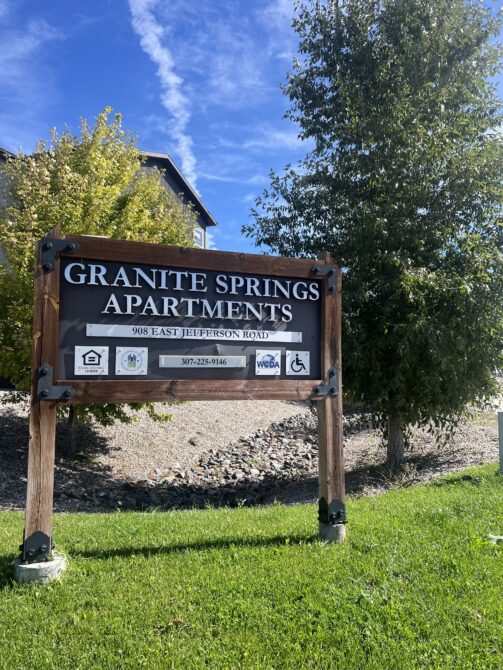 Granite Springs Apartments sign with address 908 East Jefferson Road, contact number 307-225-3146, surrounded by trees.