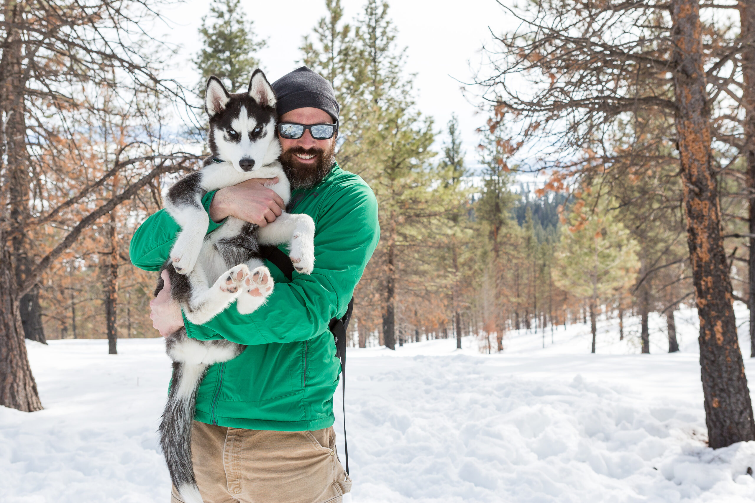 John-Sieber.jpg holding a husky puppy in snowy forest, smiling warmly