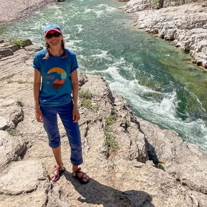 Kelly standing on rocky riverbank wearing a blue outfit, smiling.