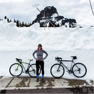 KimSieber stands in front of two bikes with snow and mountains in the background