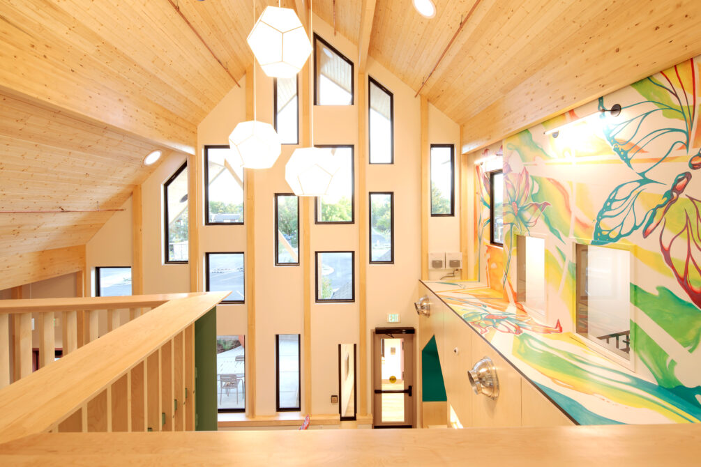 Bright modern interior with vaulted ceiling, geometric windows, and colorful abstract mural walls, showcasing natural wood elements.