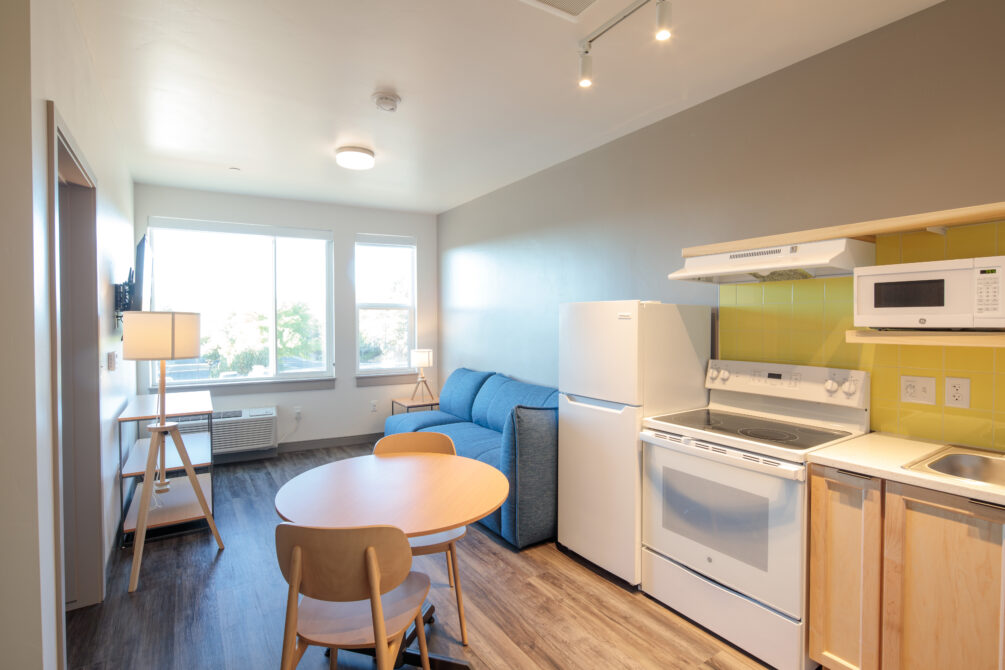 Cozy apartment interior with a blue sofa, round table, and small kitchen area.