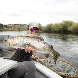 Maddy holding a large trout on a boat, smiling, river background
