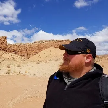 Nick Belnap looks into the distance, standing in a desert landscape with rock formations.