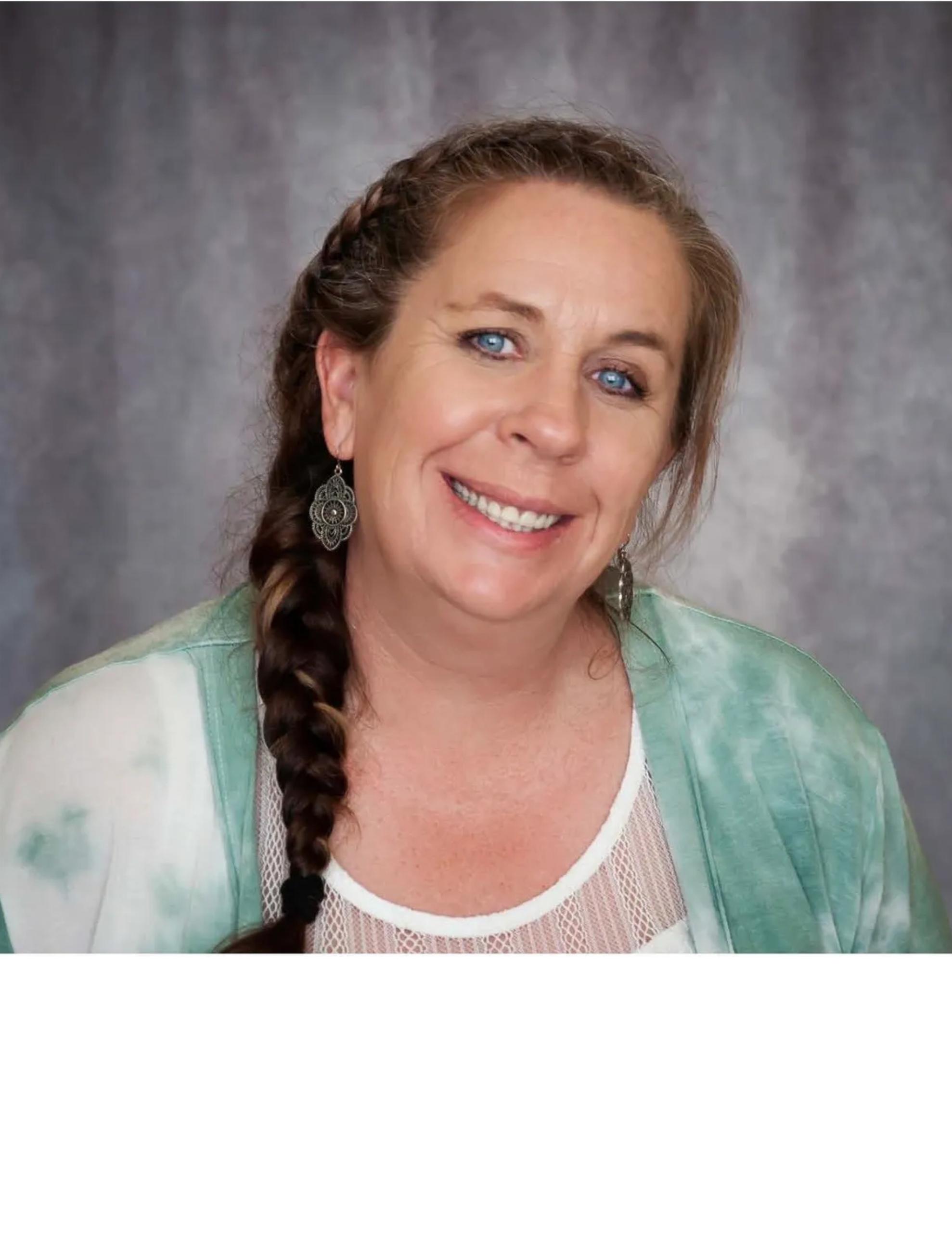 Racheal smiling, wearing green tie-dye top, braided hair, and intricate earrings, in front of a gray background.