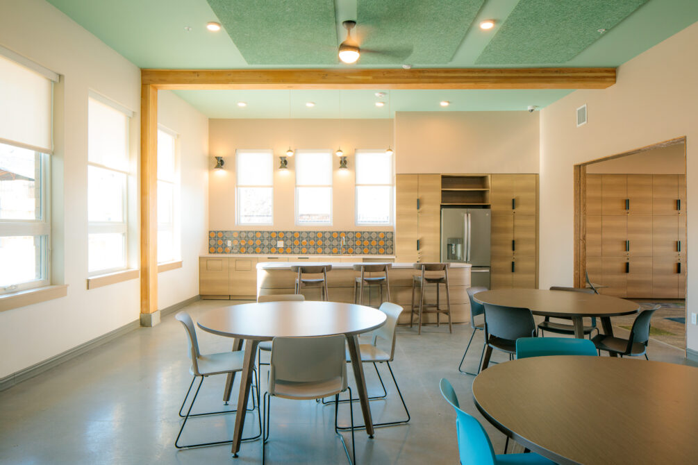 Spacious dining room with round tables, modern kitchen, and colorful tiled backsplash.