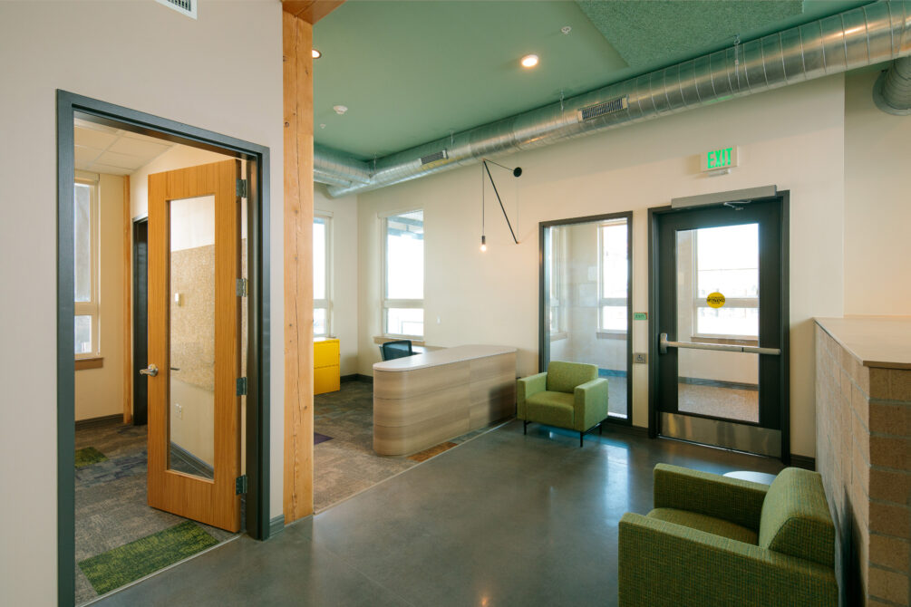 Modern office lobby with open door, green chairs, and exit signs