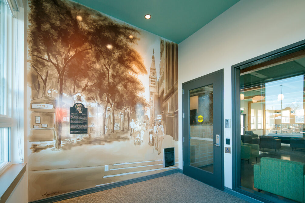 Wall mural featuring a historic street scene with trees and pedestrians, adjacent to a glass door leading to a common area