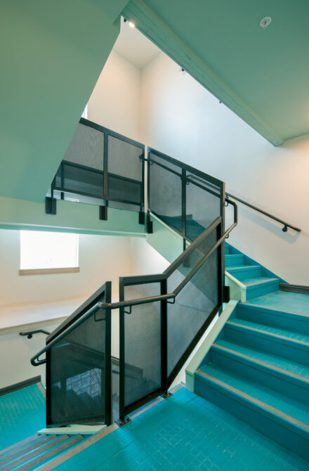 Bright turquoise stairwell with black railings and natural light from a window