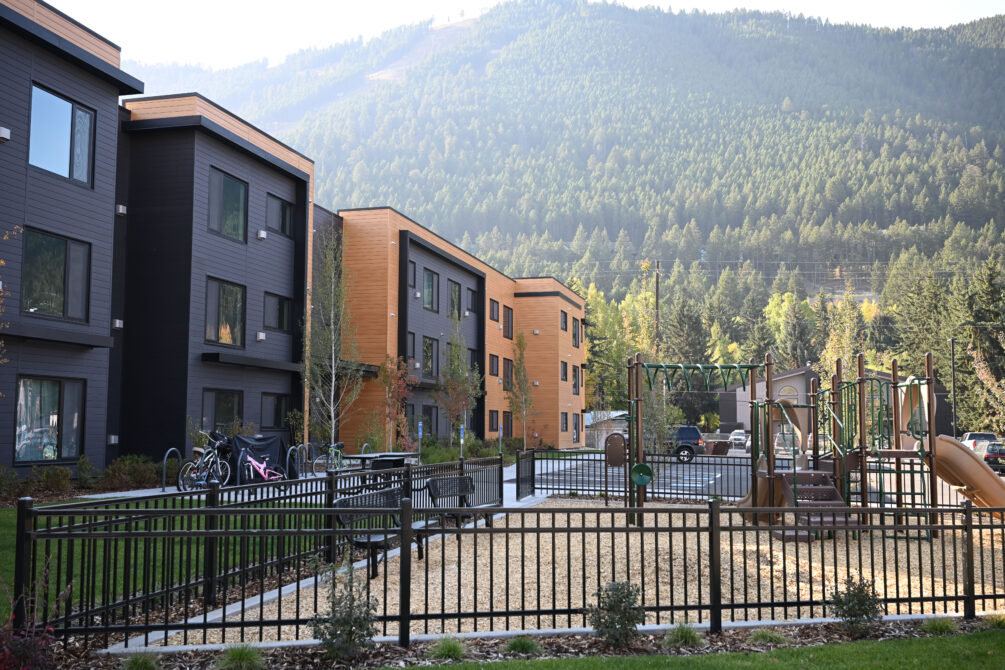 Modern apartment buildings with adjacent playground, surrounded by lush green mountains